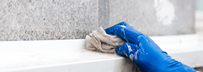A young male cleaner in blue overalls washes building's facade, windows and store front. Cleaning Service close up